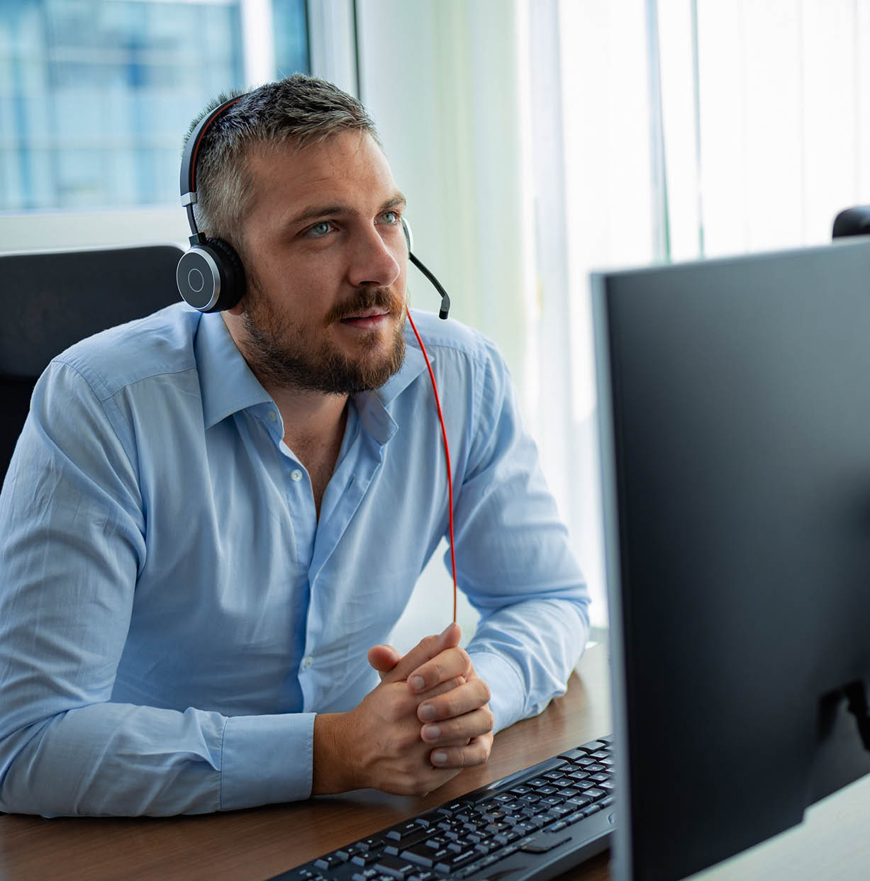 Customer service agent sitting at his office desk in front of the monitor, using webcam and headset for communication and assistance