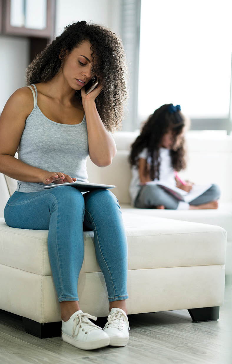 Latin woman between 25 and 35 years old is a mother working serious next to her daughter from home