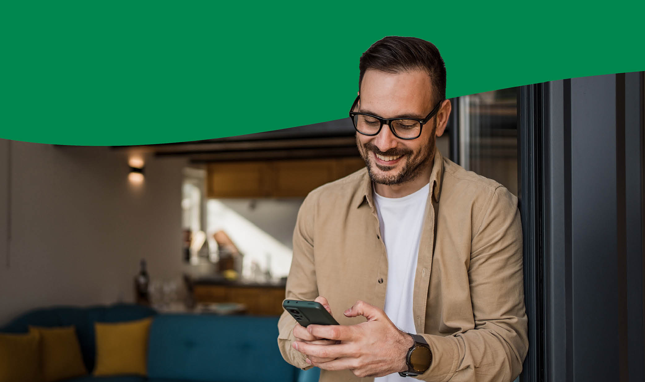 Side View Of African American Guy Using Smartphone Browsing Internet Sitting On Couch At Home. Black Man Texting On Cellphone Or Using New Application On Mobile Phone Indoors