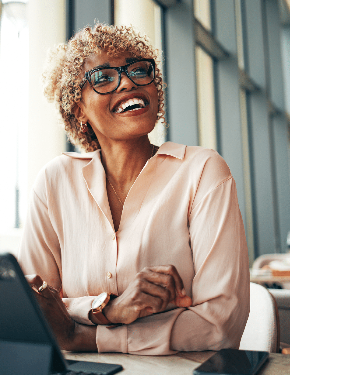 Happy African-American business woman using tablet and smartphone while sitting at restaurant desk.