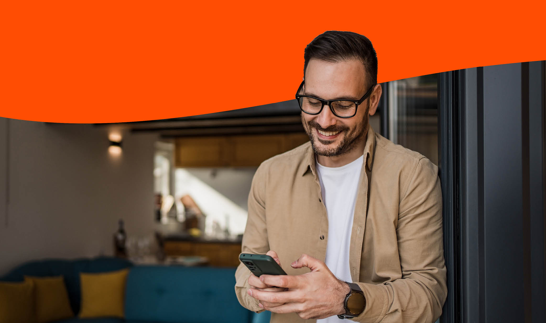 Side View Of African American Guy Using Smartphone Browsing Internet Sitting On Couch At Home. Black Man Texting On Cellphone Or Using New Application On Mobile Phone Indoors